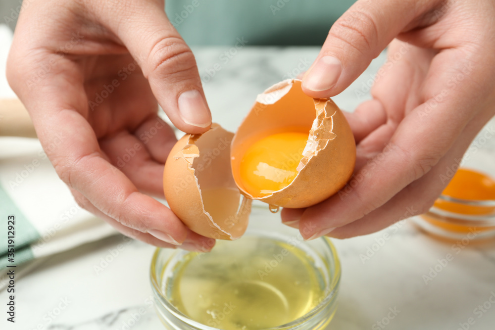 Woman separating egg yolk from white over glass bowl at table, closeup - obrazy, fototapety, plakaty 