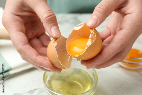 Woman separating egg yolk from white over glass bowl at table, closeup