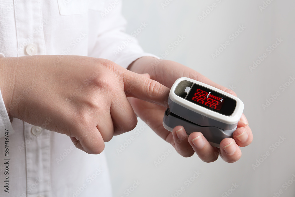 Woman using modern fingertip pulse oximeter on light background, closeup Woman using modern fingertip pulse oximeter on light background, closeup