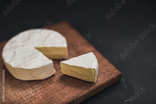Camembert round cheese and a slice lie on a wooden board. grey matte concrete background.