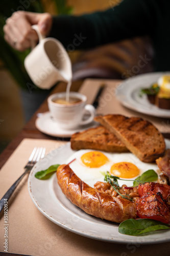 Full English breakfast - fried egg, baked beans, bacon, sausages on a dark rusty background, toasts.