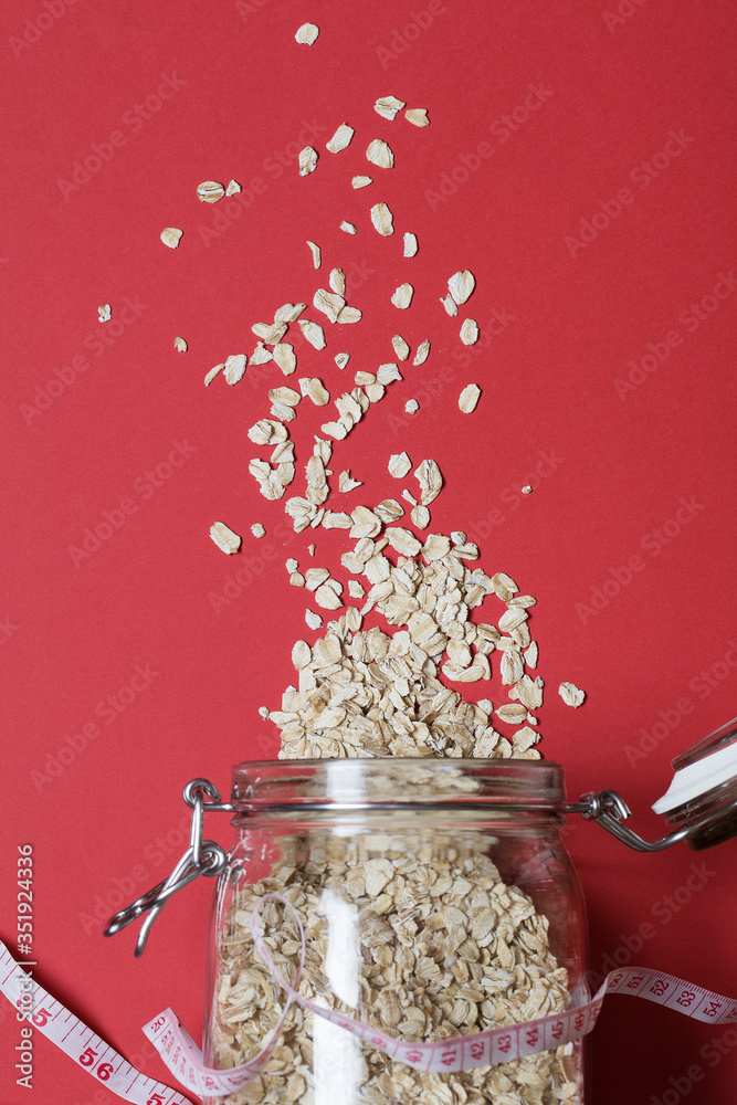 Natural oatmeal and measurement on red background . Oatmeal in a glass pot. Healthy breakfast concept .