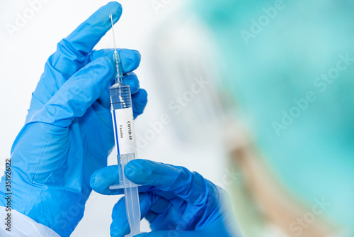 Doctor, scientist, researcher hand in blue gloves or protective suit preparing for human clinical injection trials vaccination covid-19 coronavirus vaccination Biological hazard concept.