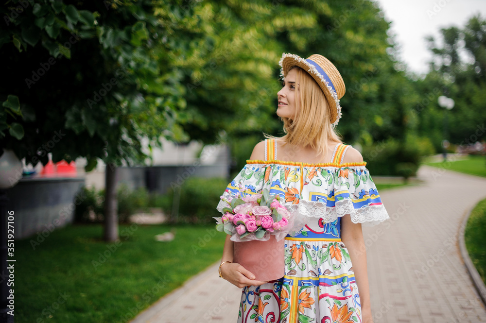 blonde woman with decorative box of flowers walks in the park
