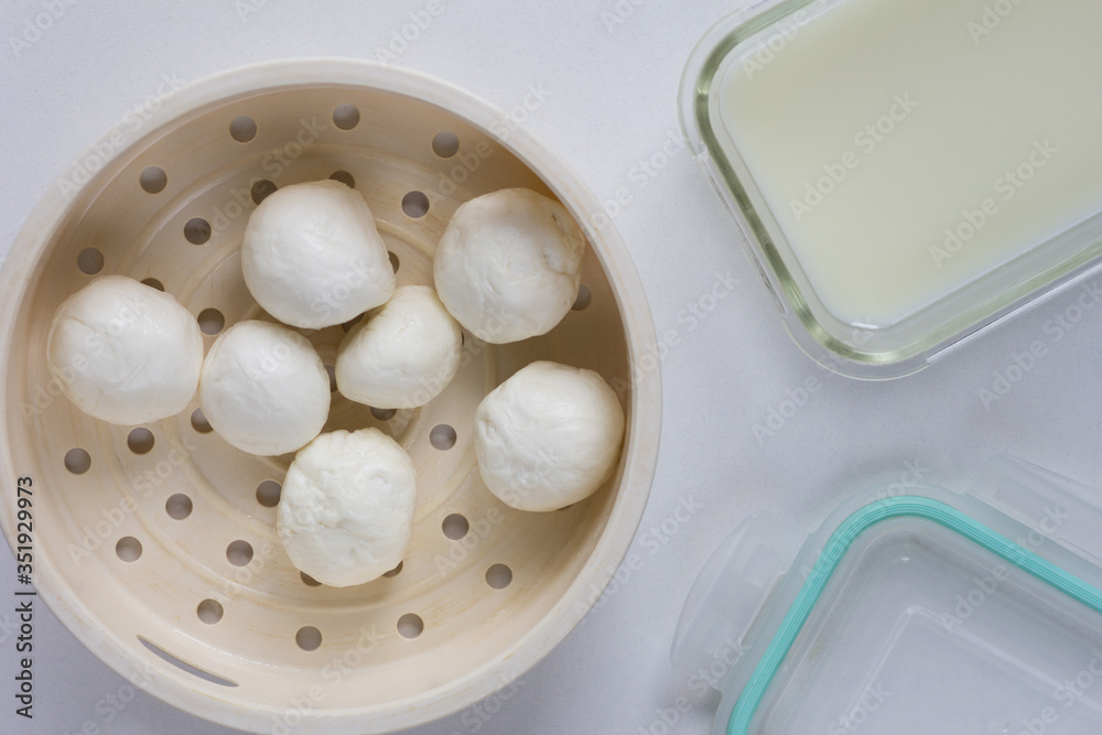 Top view of fresh homemade mozzarella balls on strainer close to whey to store cheese Top view of fresh homemade mozzarella balls on strainer close to whey to store cheese