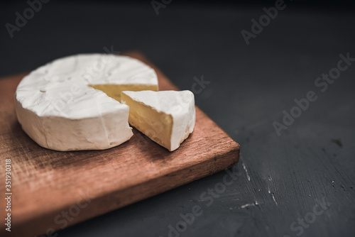 Camembert round cheese and a slice lie on a wooden board. grey matte concrete background.