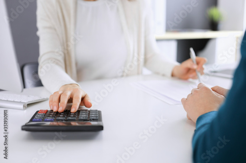 Accountant checking financial statement or counting by calculator income for tax form, hands closeup. Business woman sitting and working with colleague at the desk in office toned in blue. Tax and