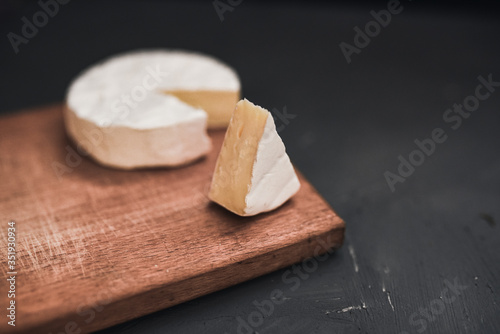 Camembert round cheese and a slice lie on a wooden board. grey matte concrete background.