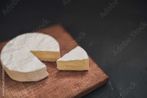 Camembert round cheese and a slice lie on a wooden board. grey matte concrete background. 