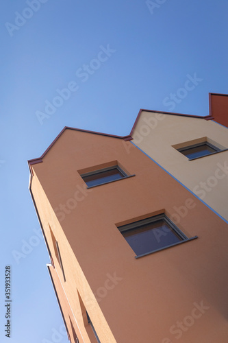 Facade of modern small residental houses being built on top of other houses in a The Netherlands. Warm colored facades in different shades. Geometric architectural style. Blue sky