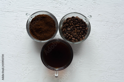 Three cups of ground coffee, coffee beans and brewed coffee in one row