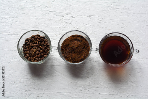 Three cups of ground coffee, coffee beans and brewed coffee in one row