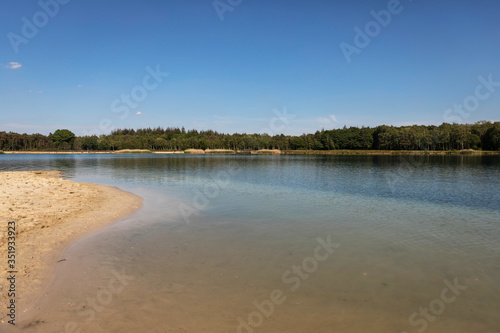 A beach lake in the Netherlands where people come to swim and sunbathe in Brabant. Calm water, greenery, sand and a blue sky. Relaxation