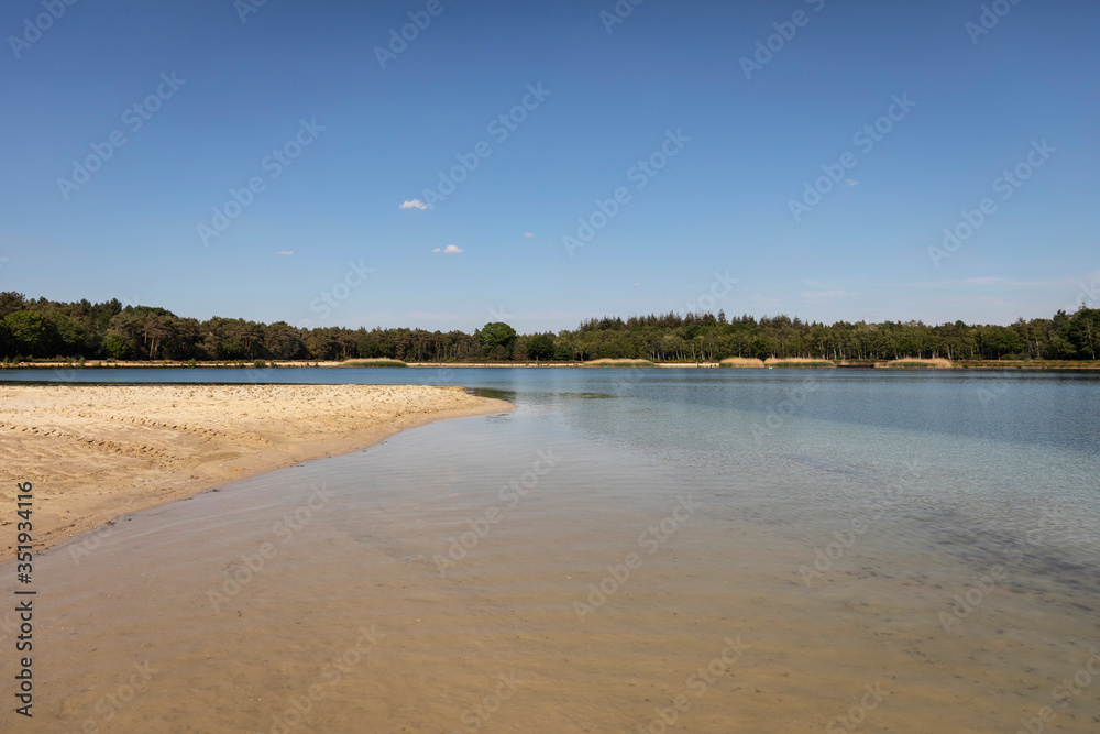A lake with a beach in the Netherlands where people come to swim and sunbathe in Brabant. Calm water, greenery, sand and a blue sky. Relaxation