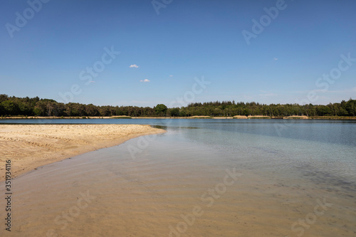 A lake with a beach in the Netherlands where people come to swim and sunbathe in Brabant. Calm water, greenery, sand and a blue sky. Relaxation
