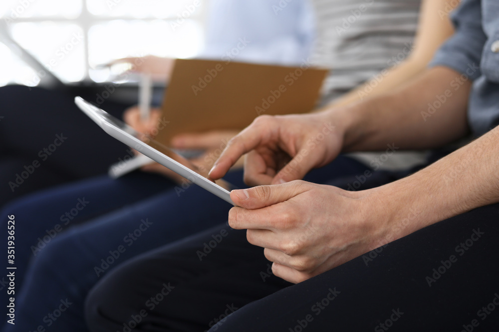 Group of casual dressed business people working at meeting or conference, close-up of hands. Businessman using tablet computer. Teamwork or coaching concept