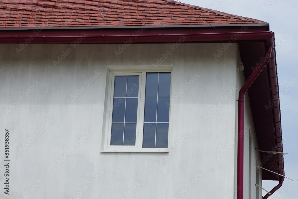 one white window on the gray wall of the house under a red tile roof