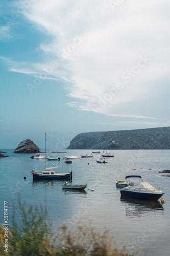 View of boats anchored on the coast with cloudy sky in Cadaques, Spain