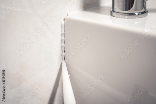 Detail of a cannula applying silicone to the seal of a bathroom sink photo