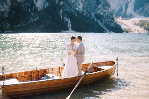 Bride and groom sailing in wooden boat, with oars at Lago di Braies lake in Italy. Wedding in Europe - Newlyweds are standing embracing in a boat. © Nadtochiy