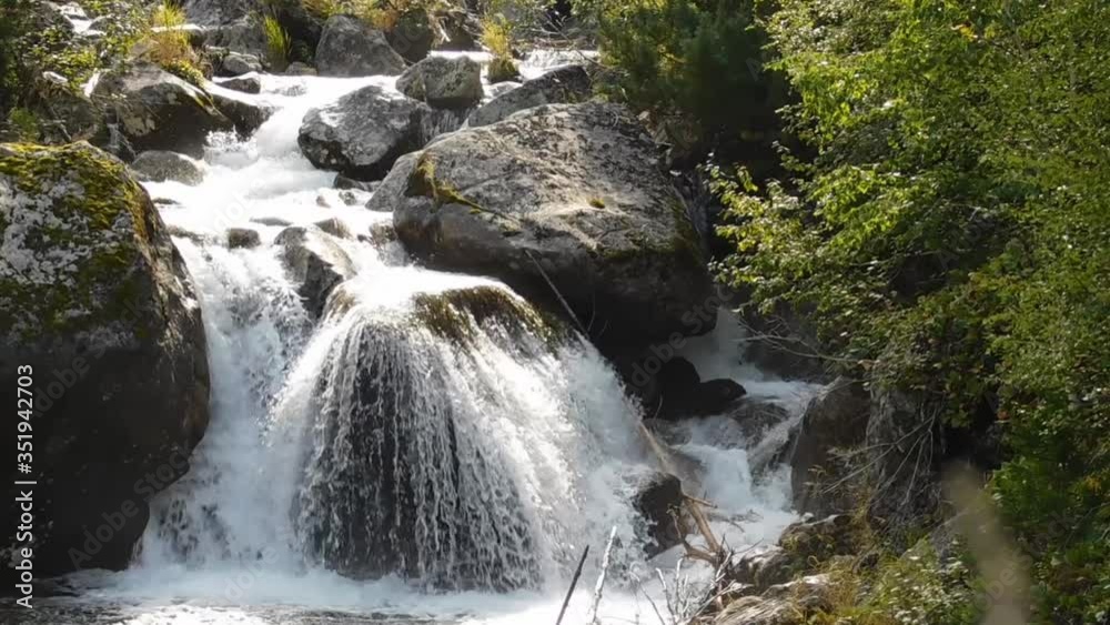 Mountain stream swiftly runs down, over huge stones, forming a beautiful waterfall Mountain stream swiftly runs down, over huge stones, forming a beautiful waterfall