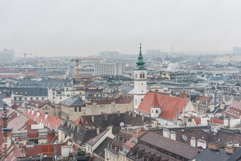 Cityscape with red tiles rooftops and church tower of the old town of Vienna in a heavy snowy day.  View at the tower of St. Stephen's Cathedral in Vienna, Austria.