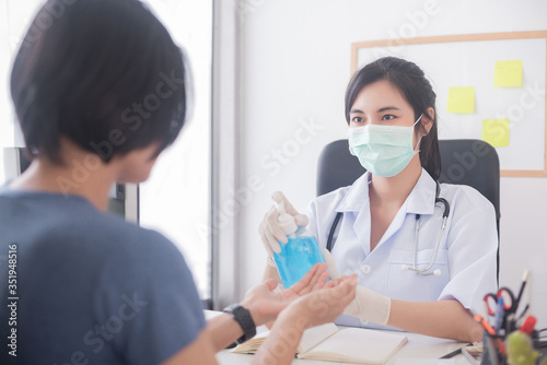 An Asian female doctor wearing a surgical mask is pouring alcohol gel on the patient s hand.