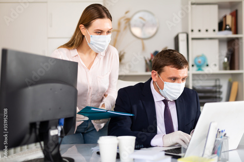 Entrepreneur in medical mask working with female coworker in office
