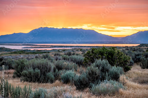Orange red yellow sunlight sunrise on Great Salt Lake in Antelope Island State Park Ladyfinger campground with reflection on water and sun rays
