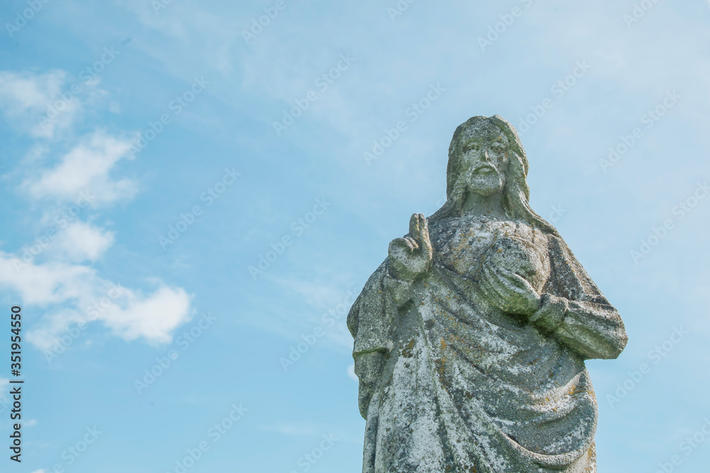 Very old stone statue of Jesus Christ against blue sky. Faith, religion, death, resurrection concept.