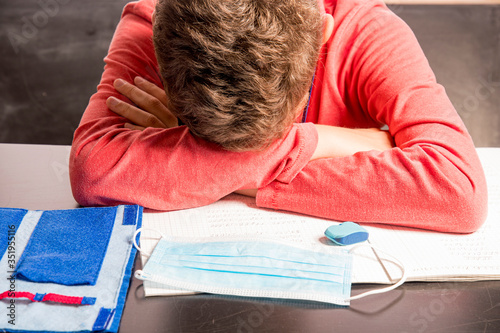 depressed boy lies on his writing materials with mouth mask in the home teaching photo