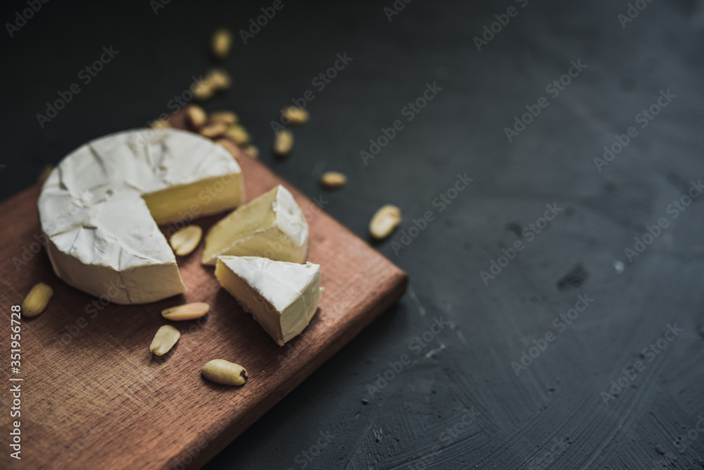 Fototapeta premium Camembert round cheese and a slice lie on a wooden board. grey matte concrete background. peanut