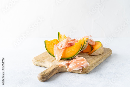 Fresh melon with prosciutto and basil. Antipasti, Italian food. Top view on white stone table with copy space for your text
