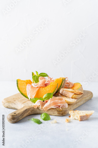 Fresh melon with prosciutto and basil. Antipasti, Italian food. Top view on white stone table with copy space for your text
