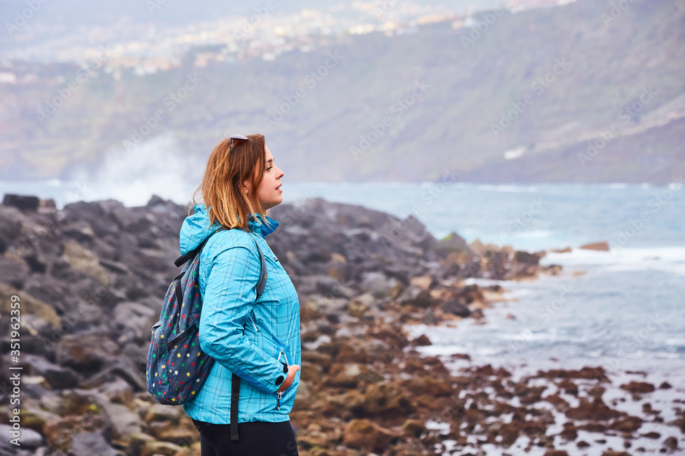 Woman tourist with backpack standing on the quay and watching the ocean in Puerto de la Cruz, The Canary Islands, Spain