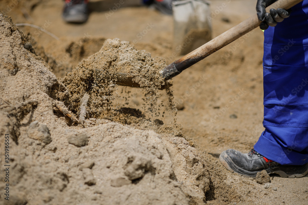 Details with a construction worker using a shovel to load sand in a wheelbarrow.