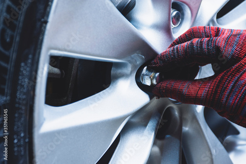 Tableau sur toile Car mechanic hand is installation wheel nuts into the alloy wheel of a car for safety