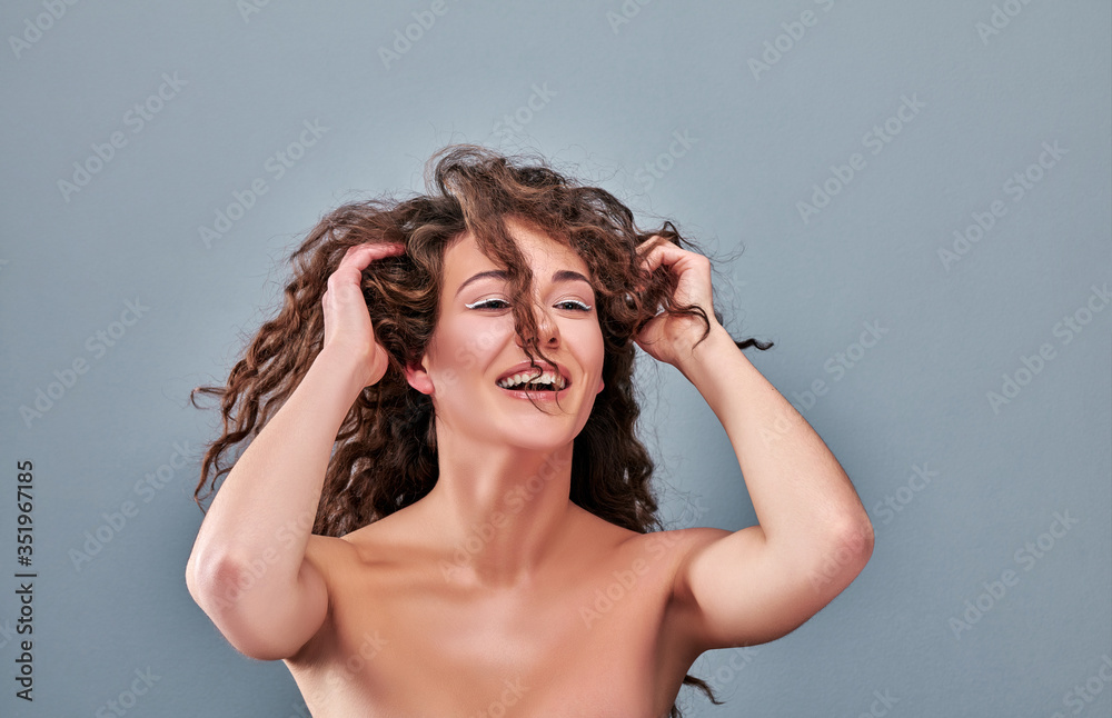 Enjoying her natural look. Close up portrait of happy smiling graceful brunette lady touching her curly hairs.