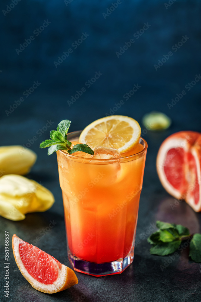 Fresh tropical cocktail with pineapple, grapefruit and ice in glass on dark blue background. Summer cold drink