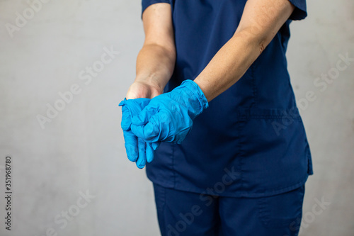 A medical health care worker woman in navy blue scrubs taking off her latex surgical gloves the correct way folding them inside out for preventing the spread of germs and disease