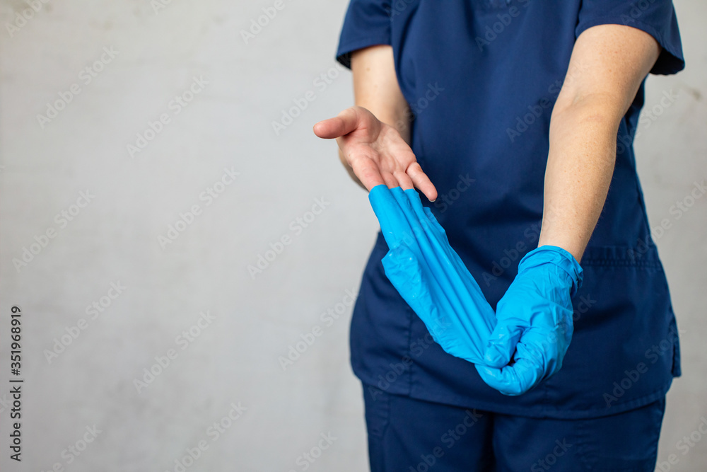 A medical health care worker woman in navy blue scrubs taking off her latex surgical gloves the correct way folding them inside out for preventing the spread of germs and disease A medical health care worker woman in navy blue scrubs taking off her latex surgical gloves the correct way folding them inside out for preventing the spread of germs and disease