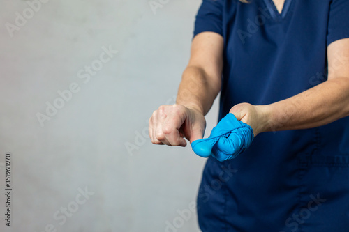 A medical health care worker woman in navy blue scrubs taking off her latex surgical gloves the correct way folding them inside out for preventing the spread of germs and disease