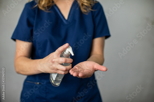 A medical health care worker woman in navy blue scrubs putting antibacterial hand sanitizer on her hands to prevent the spread of germs and disease