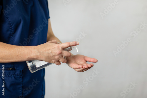 A medical health care worker woman in navy blue scrubs putting antibacterial hand sanitizer on her hands to prevent the spread of germs and disease