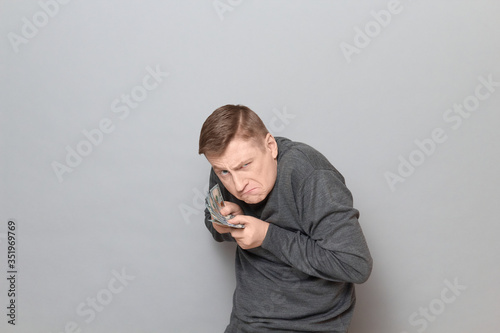 Fotografie, Obraz Portrait of funny angry greedy man holding money in hands