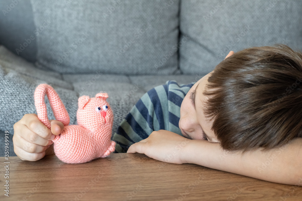 A sad child is playing with a toy pink cat made of yarn. The child plays lying on the table.