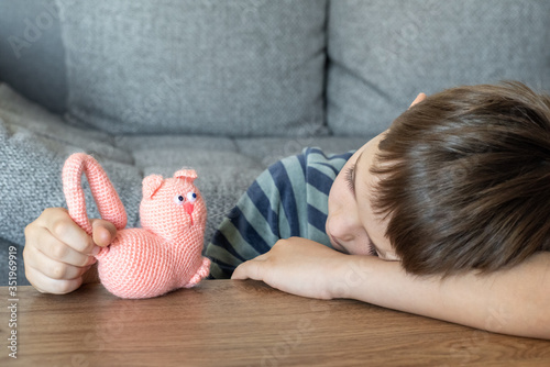 Obraz na płótnie A sad child is playing with a toy pink cat made of yarn. The child plays lying on the table. w salonie