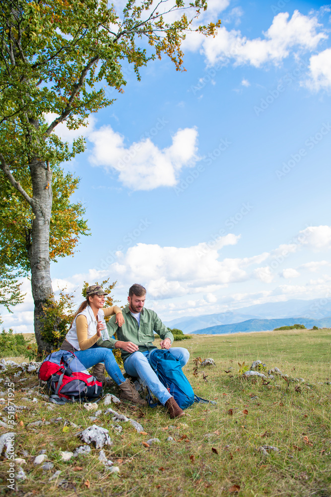 Young couple drinking water while resting on the rock during the travel in the mountains Young couple drinking water while resting on the rock during the travel in the mountains