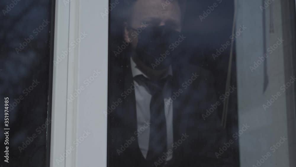 Man in a business suit stands near the window and knocks on the glass to be heard. A businessman in a mask on his face is locked in isolation. Pandemic concept. Prores 422. Man in a business suit stands near the window and knocks on the glass to be heard. A businessman in a mask on his face is locked in isolation. Pandemic concept. Prores 422.