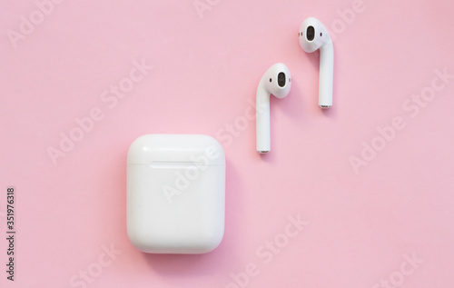 White wireless headphones are on a pink background.